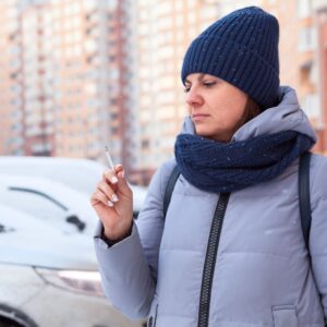 Vrouw met muts en sjaal die naar sigaret kijkt omdat ze wil stoppen met roken