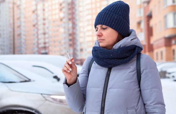 Vrouw met muts en sjaal die naar sigaret kijkt omdat ze wil stoppen met roken